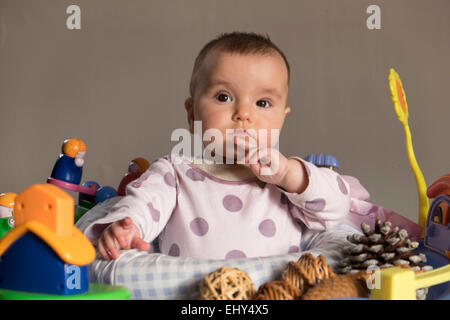 8 Monate altes Baby Mädchen, umgeben von Spielzeug in der Babywippe Stockfoto