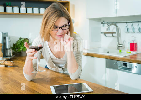 Ältere Frau hält Glas Rotwein und mit digital-Tablette Stockfoto