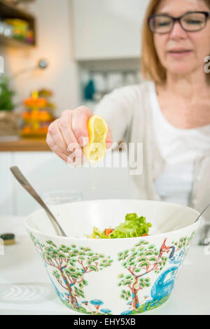 Ältere Frau geben Zitronensaft in Salat Stockfoto