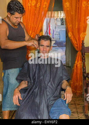 Ein kubanische Mann sitzt in der Friseur-Stuhl immer seine Haare schneiden und vorausschauend Sttraight In Havanna. Stockfoto