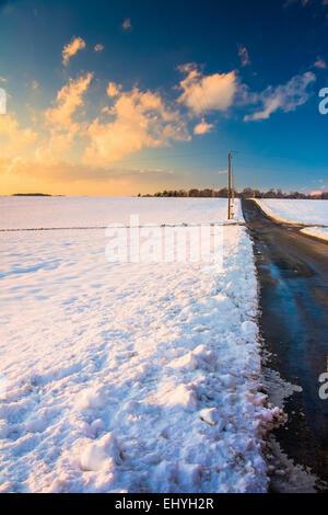 Landstraße und Schnee bedeckt Felder bei Sonnenuntergang, in ländlichen York County, Pennsylvania. Stockfoto