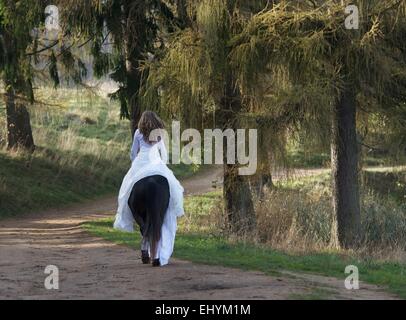 Rückansicht einer reifen Frau auf einem Pferd in einem weißen Kleid Stockfoto