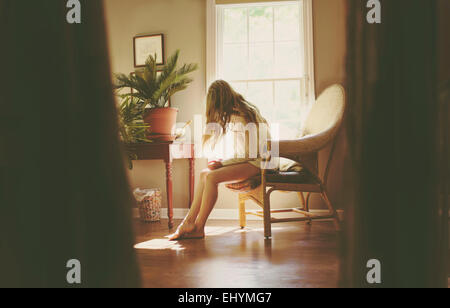 Junge Frau sitzt auf einem Stuhl im Wohnzimmer Stockfoto
