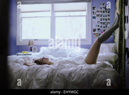 Junge Frau liegt auf ihrem Bett mit Beinen in der Luft Stockfoto