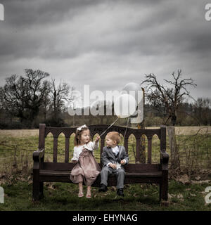 Mädchen und jungen sitzen auf einer Bank mit Luftballons Stockfoto