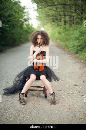 Junge Frau in einem schwarzen Kleid sitzt mit ihrer Violine Stockfoto