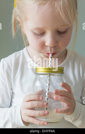 Mädchen, das Milch durch ein Stroh aus einem Einmachglas trinkt Stockfoto