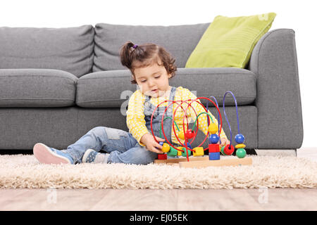 Niedliche kleine Mädchen spielen mit einem Spielzeug auf dem Boden isoliert auf weißem Hintergrund sitzend Stockfoto