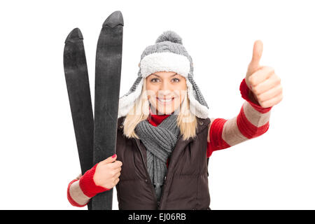 Frau in Winterkleidung hält Skier und geben oben isoliert auf weißem Hintergrund Daumen Stockfoto