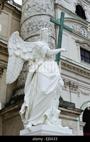 Eine Engelsstatue hält ein hölzernes Kreuz außerhalb der Karlskiche (St-Charles) Kirche, Wien, Österreich. Stockfoto