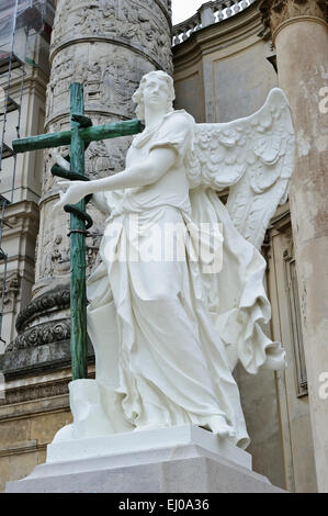 Eine Engelsstatue hält ein hölzernes Kreuz außerhalb der Karlskiche (St-Charles) Kirche, Wien, Österreich. Stockfoto