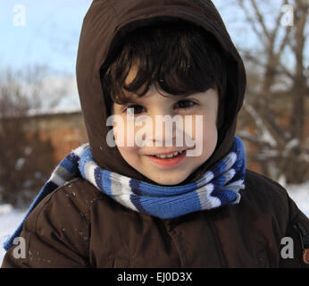 Vorschule junge mit kastanienbraunen Haaren und braunen Augen spielt in einem Wintertag mit Schnee draußen. Er ist gekleidet mit warmen Winter Tuch Stockfoto