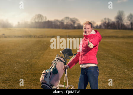 Lächelnd, glücklich attraktiven jungen Golfspielerin aufgeben einen Daumen nach Erfolg und Genehmigung Stockfoto