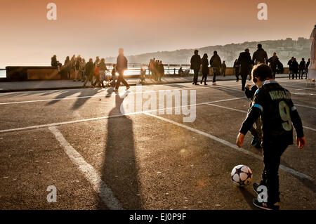 Straßenansicht der Boardwalk mit Kinder spielen Fußball bei Sonnenuntergang in Neapel, Italien. Stockfoto