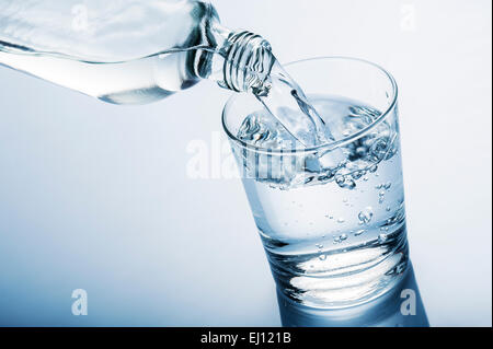 Gießen von Wasser in Glas aus einer Flasche, auf blauem Hintergrund Stockfoto