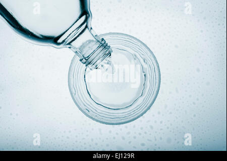 gießen Wasser in Glas aus einer Flasche, Ansicht von oben auf blauem Hintergrund Stockfoto