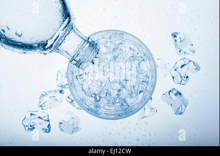 Gießen von Wasser in Glas mit Eiswürfel aus einer Flasche, auf blauem Hintergrund Stockfoto