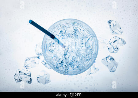 Glas voll mit frischem Wasser mit Eiswürfeln und dünnen Rohrstock auf blauem Hintergrund Stockfoto