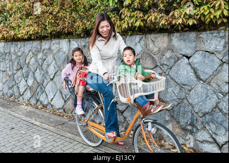 Kyoto, Japan. Eine junge japanische Mutter auf einem Fahrrad mit ihren zwei kleinen Kindern in Sitze auf Vorder- und Rückseite Stockfoto