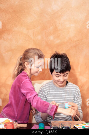 Jungen und Mädchen, die Ostereier am Tisch zu Hause. Orange gebürstet Wand als Raum für Text im Hintergrund Stockfoto