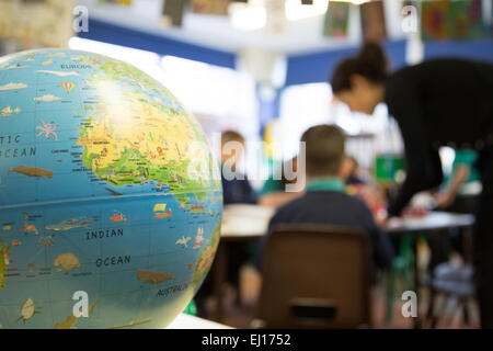 Lehrer in einem UK-Grundschule-Klassenzimmer mit einem Globus im Vordergrund Stockfoto