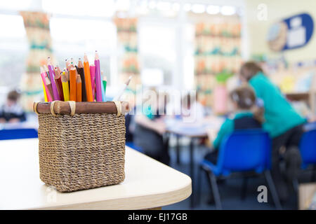 Schülerinnen und Schüler in einem UK-Grundschule-Klassenzimmer mit einem Topf Buntstifte im Vordergrund. Stockfoto