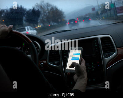 In dem Auto texting Fahrerin in l/h Fahrzeug fahren heimlich SMS-Smartphones während der Fahrt auf langen nassen Autobahn bei Dämmerung Stockfoto