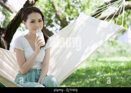 Junge Frau sitzt auf der Hängematte und Flasche Milch trinkt, Stockfoto