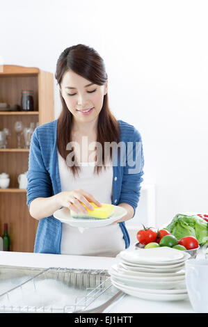 Junge Frau waschen Platten in der Küchenspüle mit Lächeln, Stockfoto