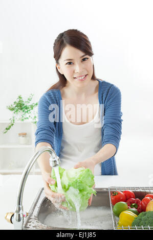 Junge Frau waschen Gemüse in die Spüle und lächelt in die Kamera, Stockfoto