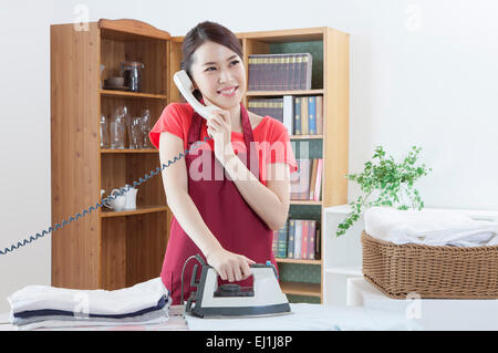 Junge Frau Kleidung bügeln und am Telefon mit Lächeln, Stockfoto