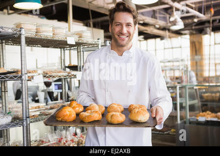 Fröhliche Bäcker hält Tablett mit Brot Stockfoto