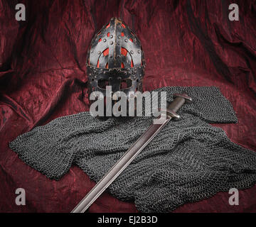 Mittelalterliche Rüstung, Helm und Schwert, rote Leinwand Hintergrund Stockfoto