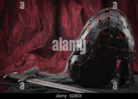 Mittelalterliche Rüstung, Helm und Schwert, rote Leinwand Hintergrund Stockfoto