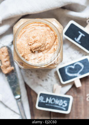 Vertikale Foto von hausgemachten natürliche Mandel-Butter in einem Glas auf rustikale Beige Tischdecke gelegt. Ansicht von oben. Stockfoto