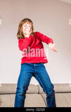 Kleines Mädchen singt mit einem Kamm stehen auf dem sofa Stockfoto