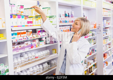 Lächelnde Apotheker telefonieren und Einnahme von Regal Stockfoto