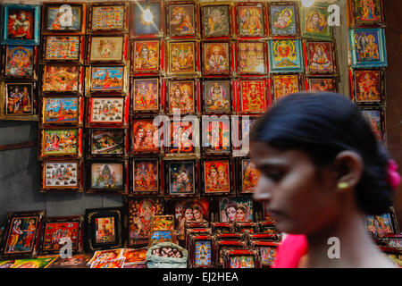 Frau geht vor dem Bilderladen der Götter in einer der Gassen von Varanasi, Indien, vorbei. Stockfoto