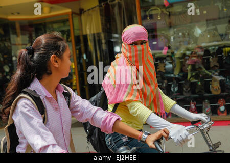 Ein Schulmädchen, das einen Hijab trägt und ein Gespräch mit einem Freund führt, während sie während eines Staus in Varanasi, Uttar Pradesh, Indien, Fahrrad fahren. Stockfoto