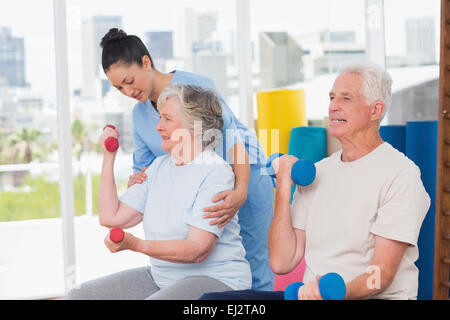 Lehrer, die Unterstützung von senior Frau beim Heben der Hanteln von Mann Stockfoto