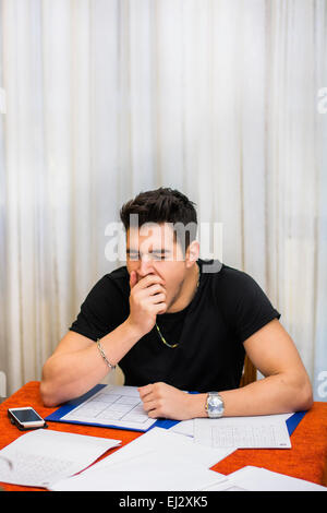 Müde, erschöpft oder mutlos junger Mann sitzt an einem Tisch mit einem Ordner der Papierkram Gähnen Stockfoto