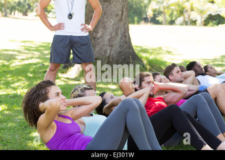 Fitness-Gruppe macht Sit-Ups im Park mit Trainer Stockfoto