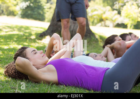 Fitness-Gruppe macht Sit-Ups im Park mit Trainer Stockfoto