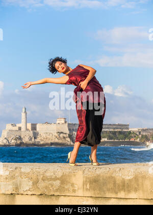 26-jährige Hispanic kubanischen weibliches Model posiert in braunen Kleid an der Malecón Wand mit historischen Morro Schloß im Hintergrund. Stockfoto