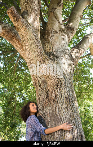 Hübsche junge Frau umarmt einen Baum Stockfoto