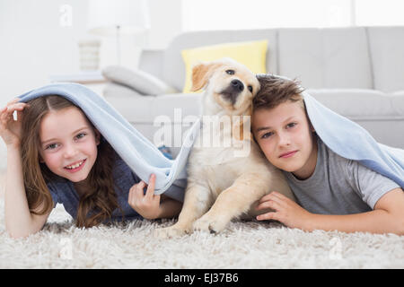 Niedlichen Geschwister mit Hund unter der Decke im Wohnzimmer Stockfoto