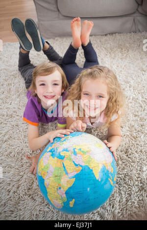 Bruder und Schwester mit Globus auf Teppich liegend Stockfoto