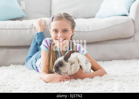 Glückliches Mädchen mit Kaninchen auf Teppich im Wohnzimmer liegen Stockfoto