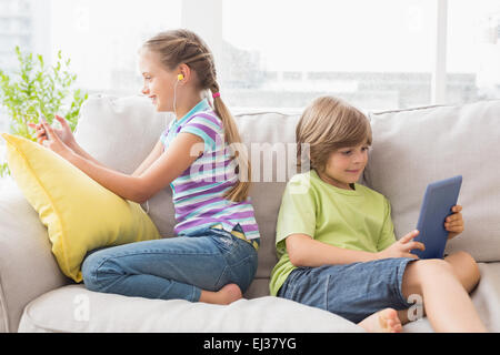 Geschwister, die mit Technologien auf sofa Stockfoto