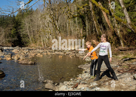 Neun Jahre altes Mädchen und sieben Jahre alten Jungen werfen von Steinen in den Snoqualmie River in der Nähe von North Bend, Washington, USA Stockfoto